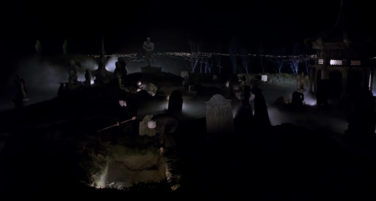 The Addams Family (1991) movie still: wide — A night landscape features a fog-covered burial site with numerous stone grave markers. Several figures…