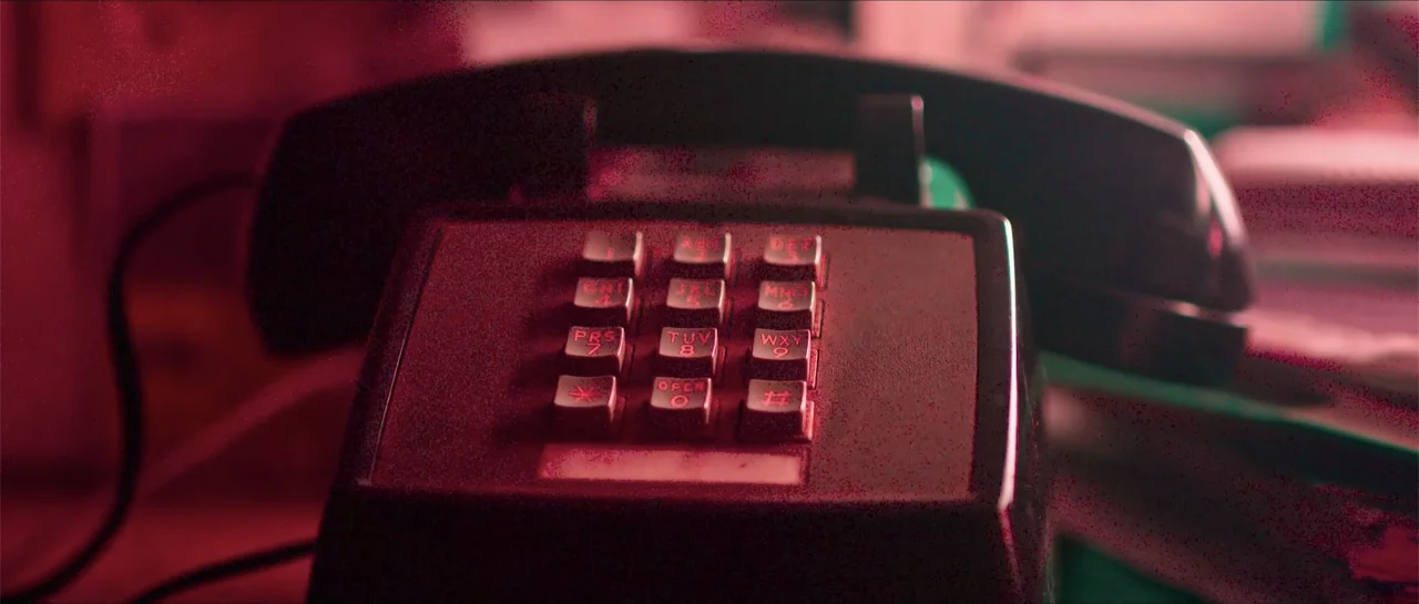 68 Kill (2017) movie still: closeup — A vintage push-button desk telephone sits on a darkened surface. The device is bathed in intense red light.