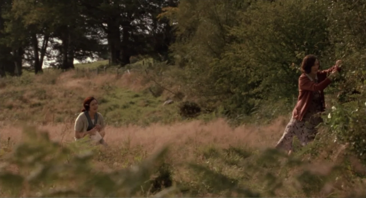 Dancing at Lughnasa (1998) movie still: wide — A sprawling rural hillside features dry tall grasses and dense distant trees. One woman kneels in the…