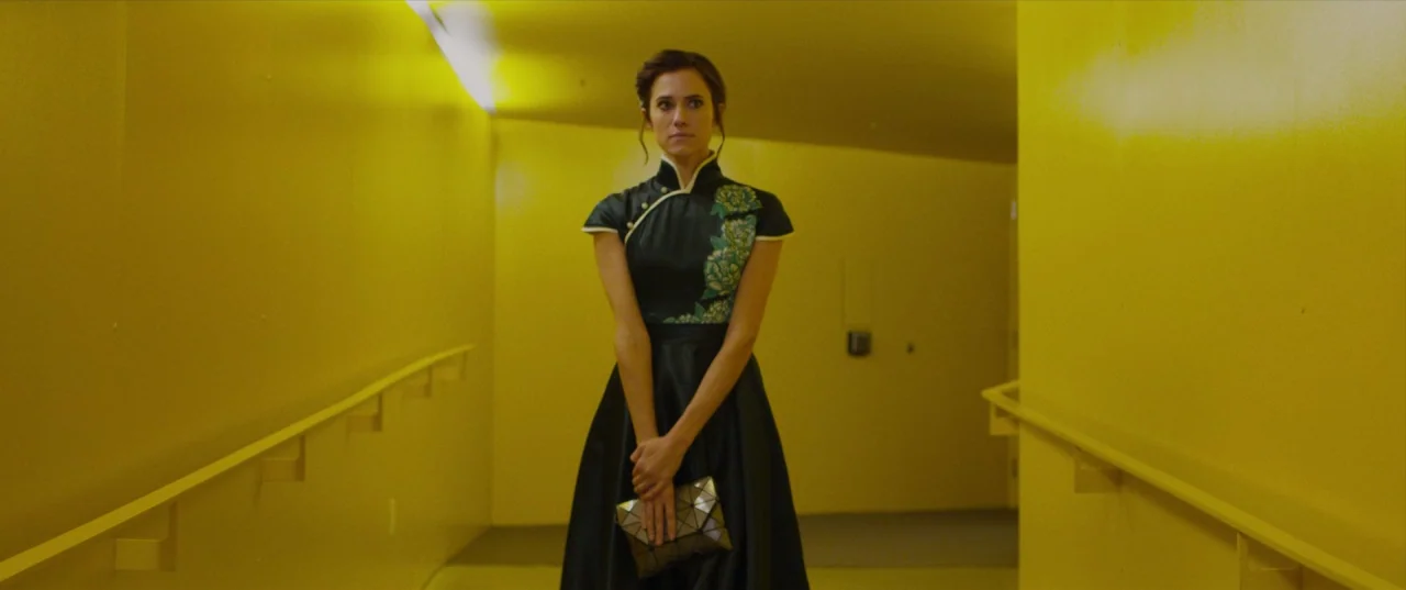 The Perfection (2018) movie still: medium — A stark corridor features intense yellow walls and matching handrails on both sides. A woman stands in…
