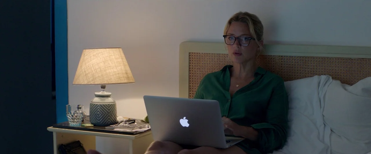 Sibyl (2019) movie still: medium — A bedroom at night with a wicker headboard and a bedside table lamp glowing. A woman in a green shirt sits in bed…