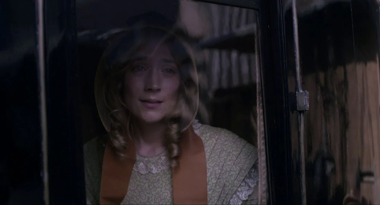 Ammonite (2020) movie still: closeup — The interior of a period-accurate dark carriage features glass panels and paneled wood walls. A woman with…