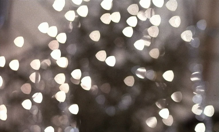The Man Who Loved Women (1977) movie still: closeup — A field of soft white light bokeh points overlaps across the dark background. The circular and…