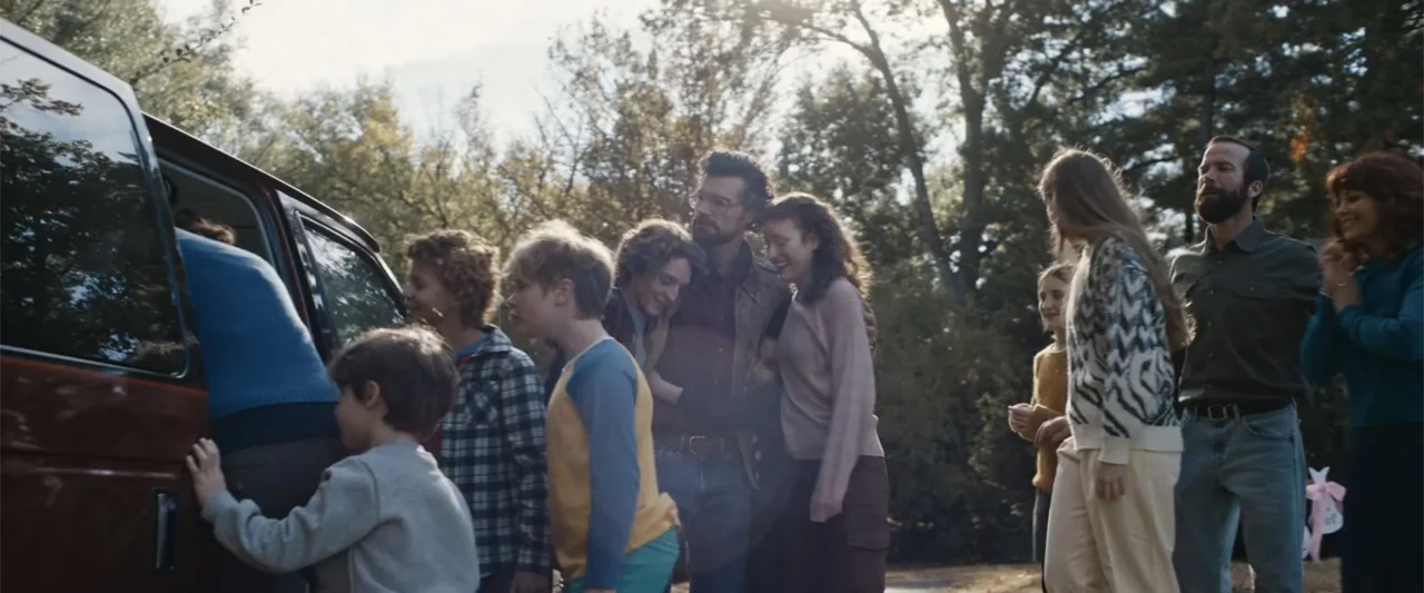 Unsung Hero (2024) movie still: wide — A group of diverse individuals stands near an open van in a tree-lined driveway. People of various ages…