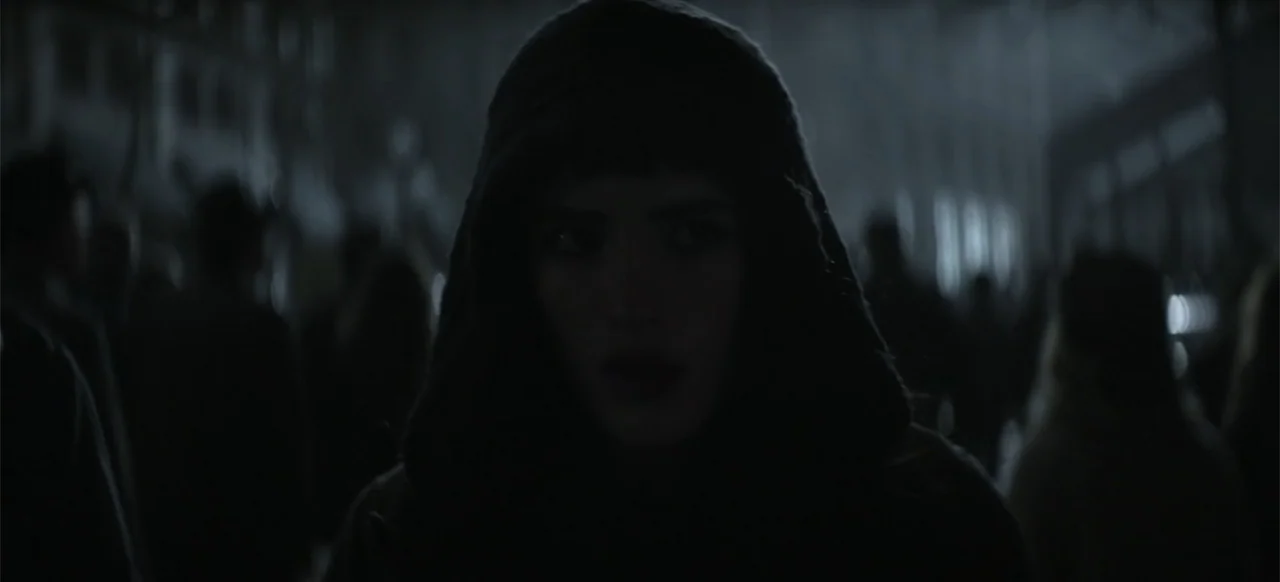 I Still See You (2018) movie still: closeup — An outdoor nighttime space filled with blurred figures of a crowd. A young woman in a hood stands in…