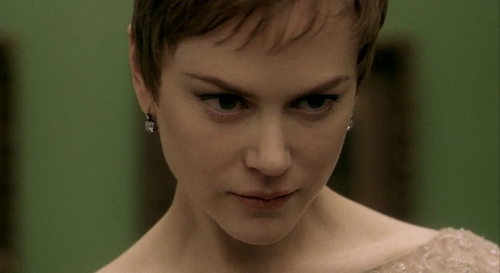 Birth (2004) movie still: closeup — A close-up of a woman in front of a muted green wall. She is looking slightly downward while her face is lit by…