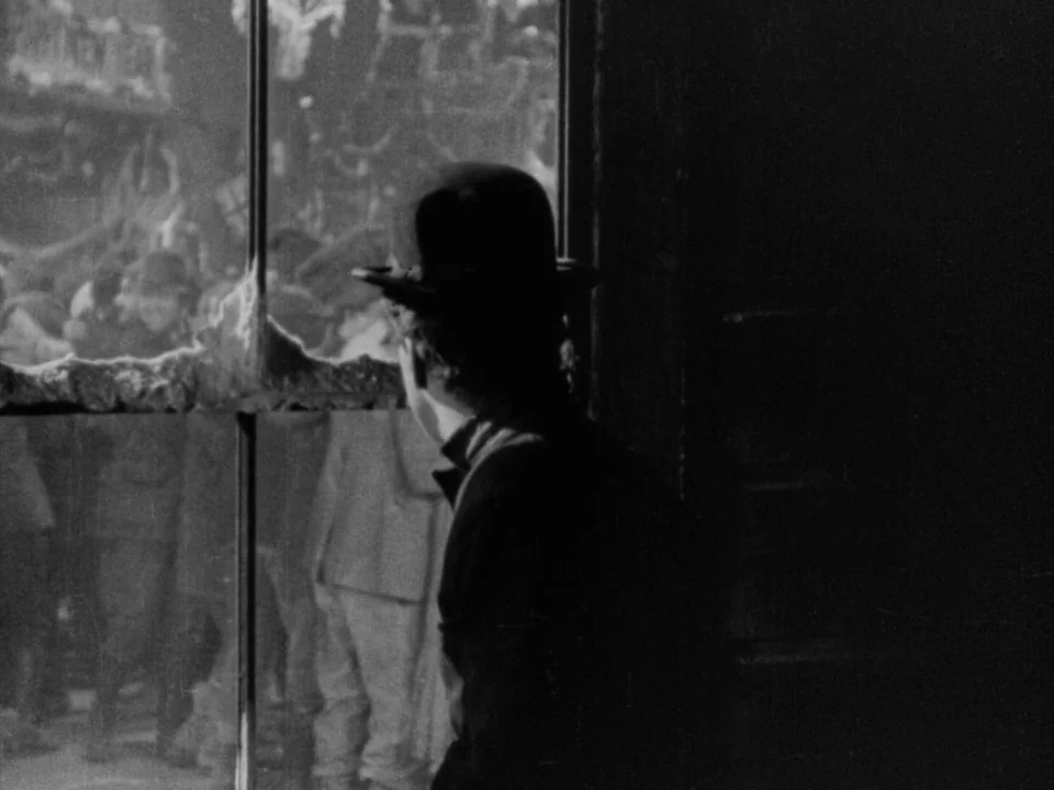 The Gold Rush (1925) movie still: medium — An interior space with a dark foreground containing a figure near a window frame. The window shows a…