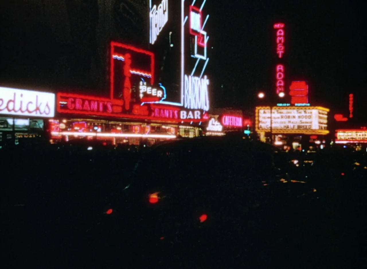 The Band Wagon (1953) movie still: wide — A night view of a busy city street illuminated by numerous vibrant neon signs. A dark car silhouette…