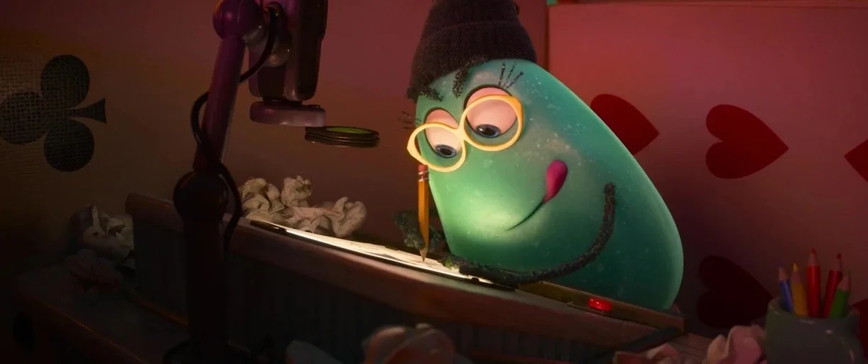 Inside Out 2 (2024) movie still: medium — A teal blob character sits at a desk in a room with pink walls. The character works on a drawing under the…