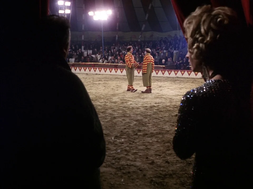 The Clowns (1970) movie still: medium — A view from behind an audience member looking into a large circus arena. Two clowns perform in the center…