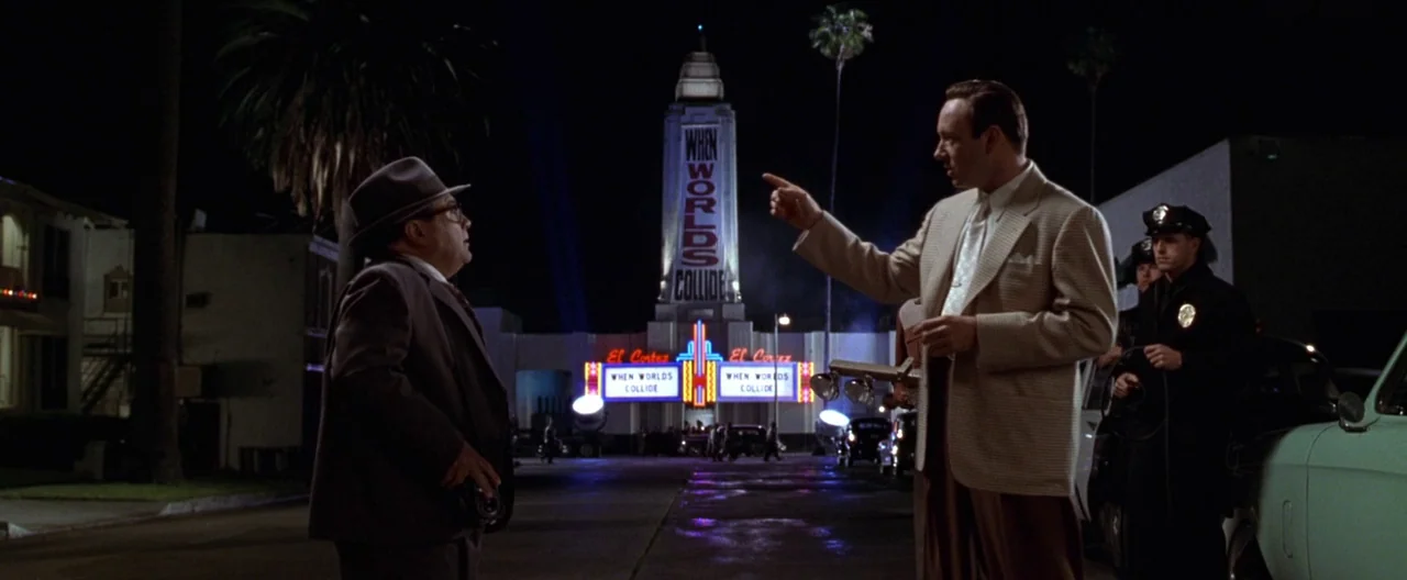 L.A. Confidential (1997) movie still: wide — An empty nighttime street features a glowing marquee for a film titled When Worlds Collide. Two men…