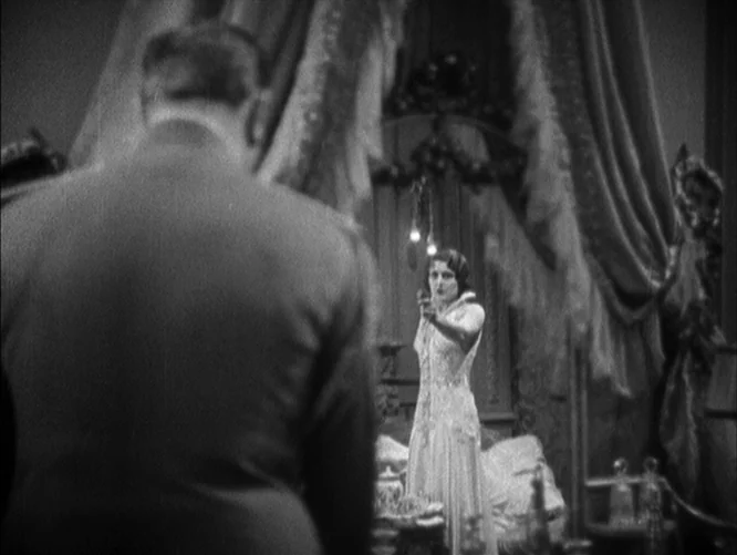 The Last Command (1928) movie still: medium — A dark boudoir features heavy draped curtains and ornate furniture in the background. A woman stands…