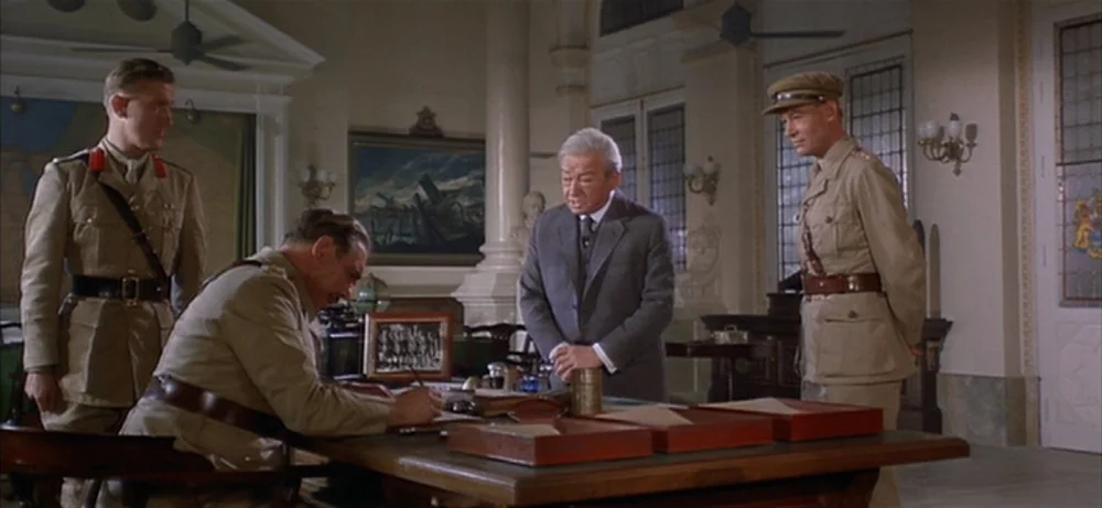 Lawrence Of Arabia movie still: medium — A spacious formal room features a large desk with documents and wall-mounted maps. Four men in military and…