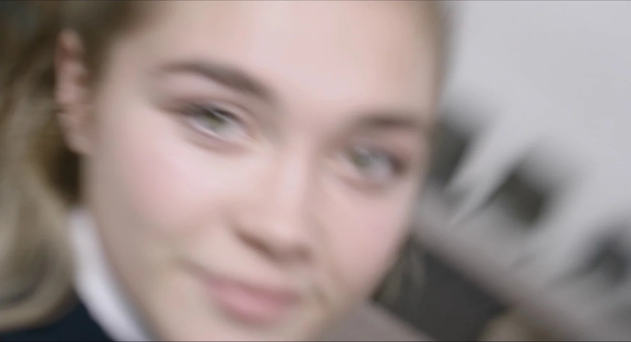 The Falling movie still: closeup — A close-up of a young woman inside an indoor space with blurred background elements. The subject moves her face…