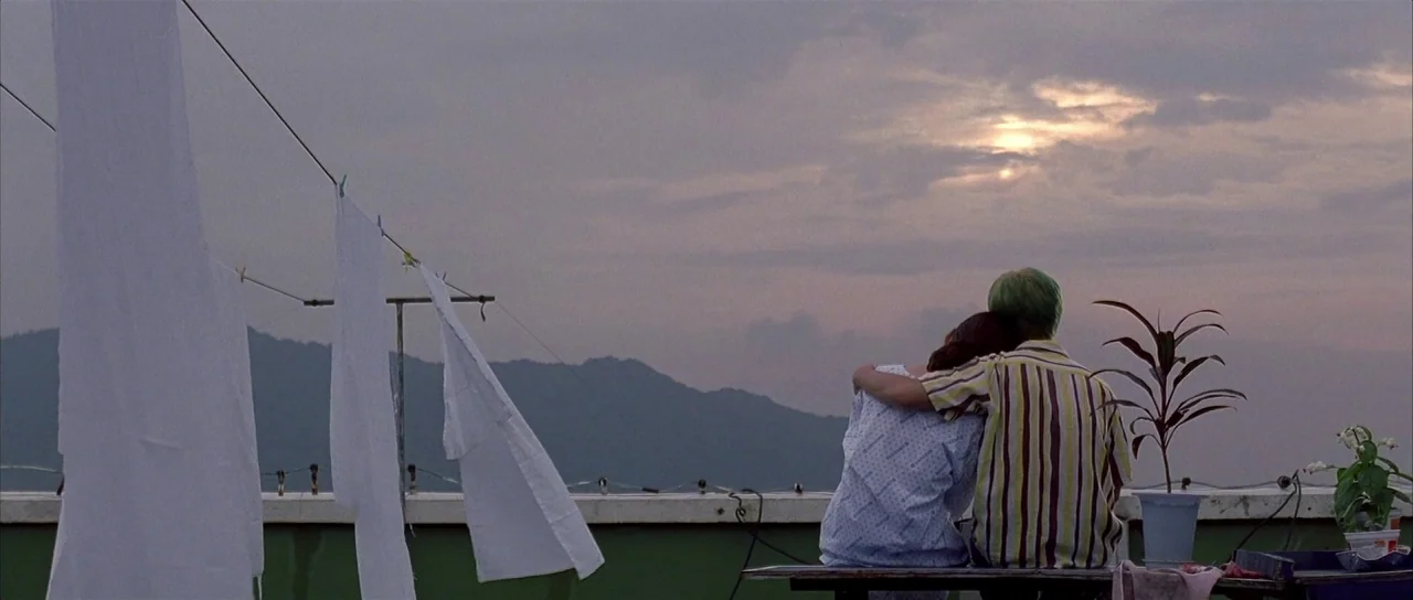 Sympathy for Mr. Vengeance (2002) movie still: wide — A flat rooftop overlooks distant mountain ridges under a clouded evening sky. A couple sits on…