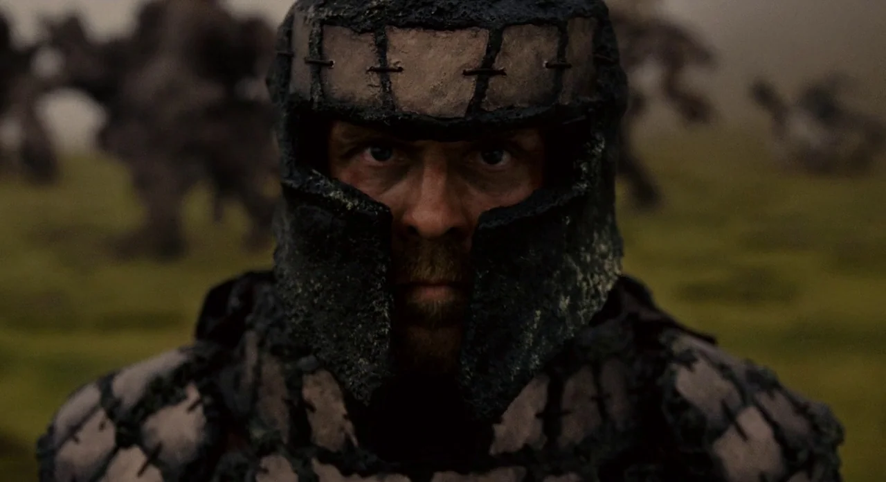 Noah (2014) movie still: closeup — A man in textured, dark handmade armor stands in an open, foggy field. The subject looks forward with intense…