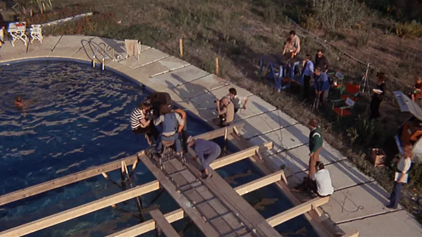 Day for Night (1973) movie still: wide — A film crew operates a camera on a wooden dolly track spanning a pool. Multiple production staff observe…