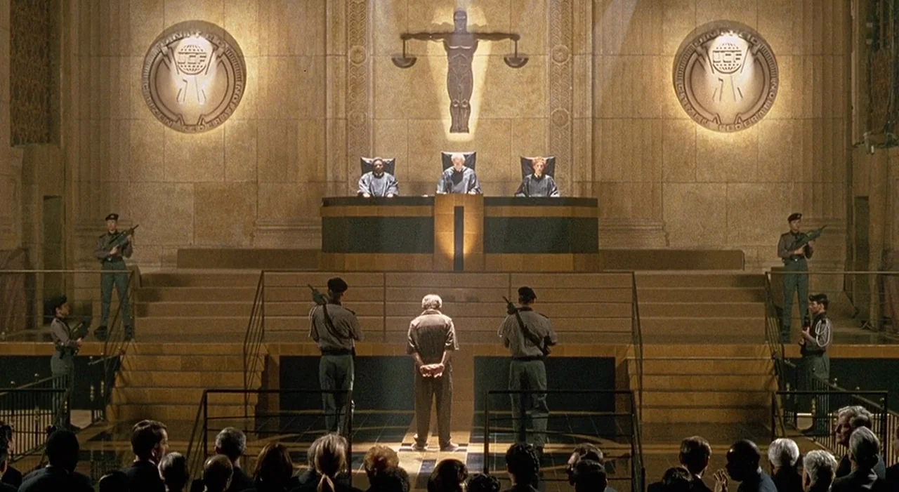 Starship Troopers (1997) movie still: wide — A high-ceilinged futuristic courtroom features large stone walls adorned with metallic geometric…