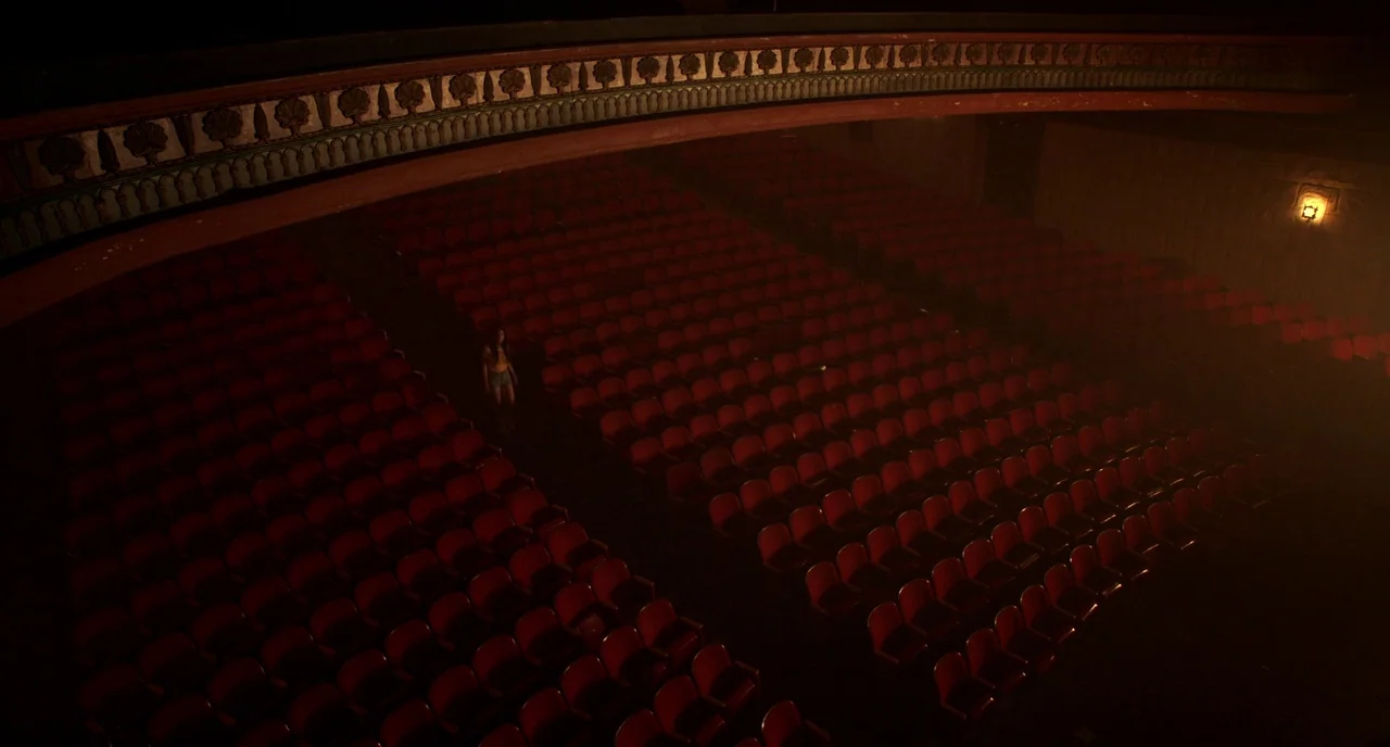 Nightmare Cinema movie still: wide — A dark, empty movie auditorium features many rows of red cushioned seats. A lone woman stands in the middle…