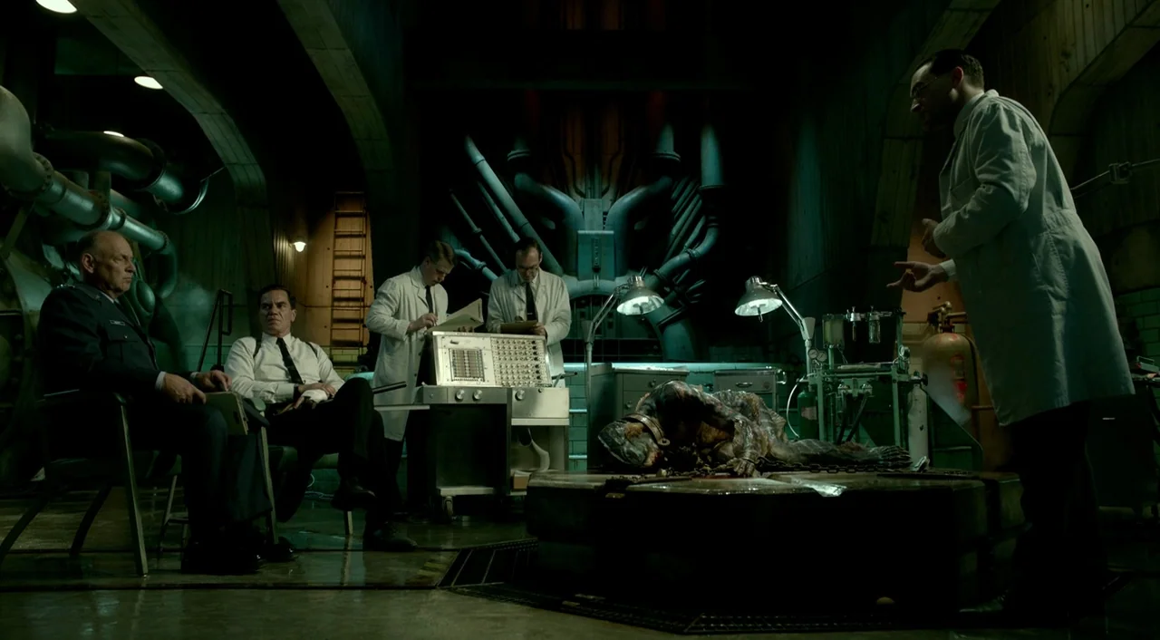 The Shape of Water (2017) movie still: wide — A dark, industrial concrete research facility features exposed piping and a central metal platform.…