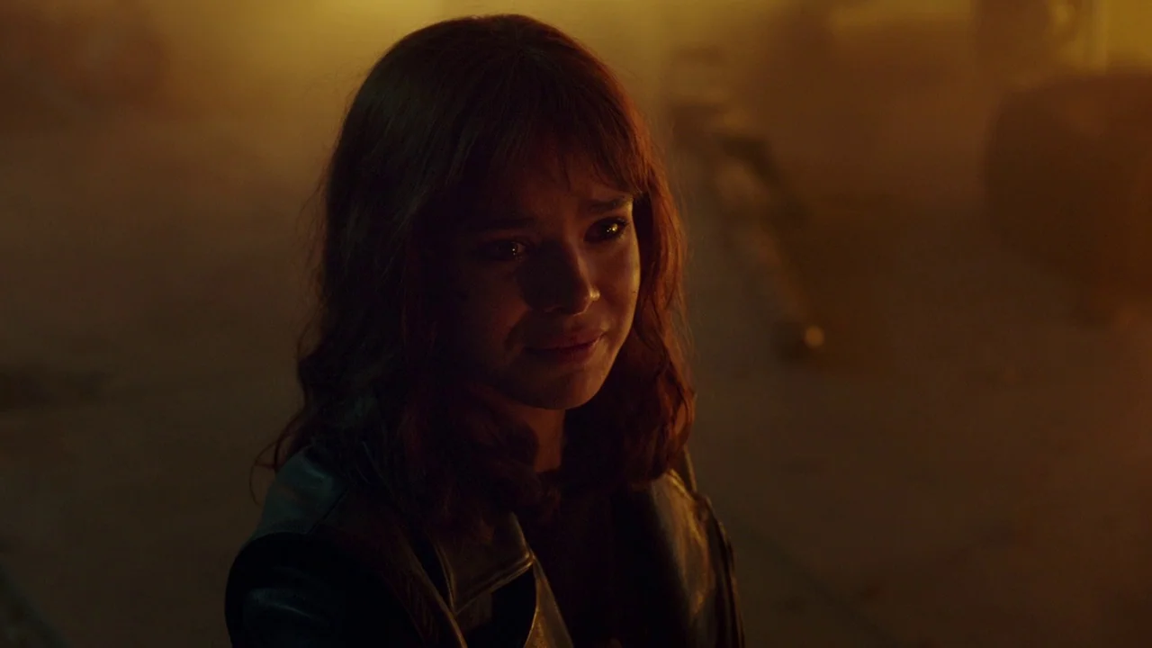 Bumblebee (2018) movie still: closeup — A dark outdoor alleyway is filled with thick, warm, hazy light. A young woman with teary eyes looks forward…
