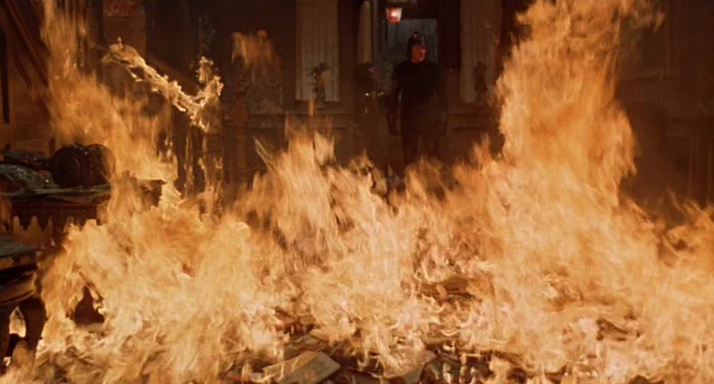 Fahrenheit 451 (1966) movie still: wide — A grand, dark manor interior is overtaken by a large, spreading fire. A lone man stands in the distant…