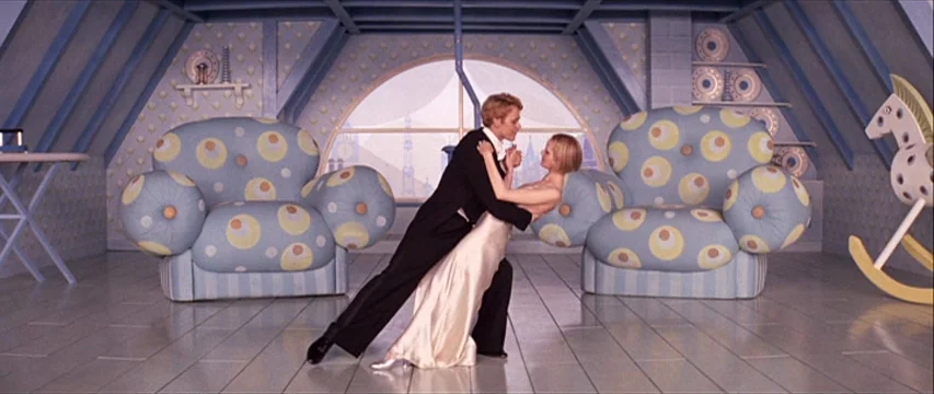 The Boy Friend (1971) movie still: fullbody — An attic room features blue patterned wallpaper and two large rounded armchairs. A man in a tuxedo…