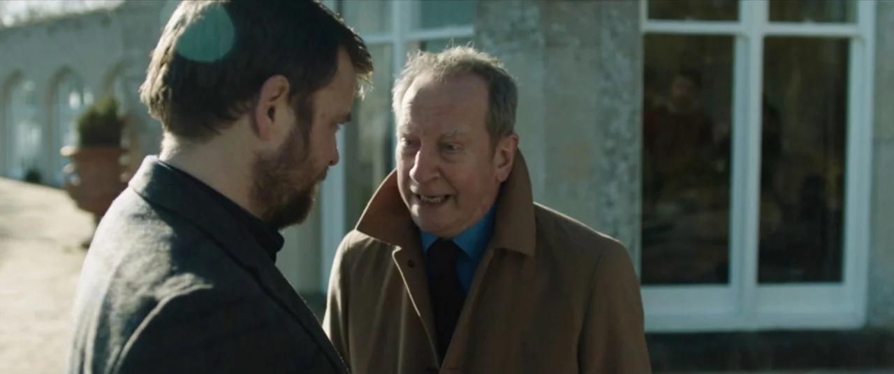 Happy New Year, Colin Burstead (2018) movie still: medium — An outdoor stone patio adjacent to a large country house with glass doors. Two men stand…