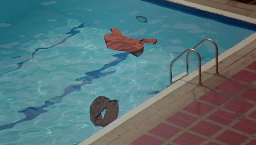 Last Life in the Universe (2003) movie still: wide — A turquoise swimming pool features red tiles along the edge with metal steps. A shirt and pants…