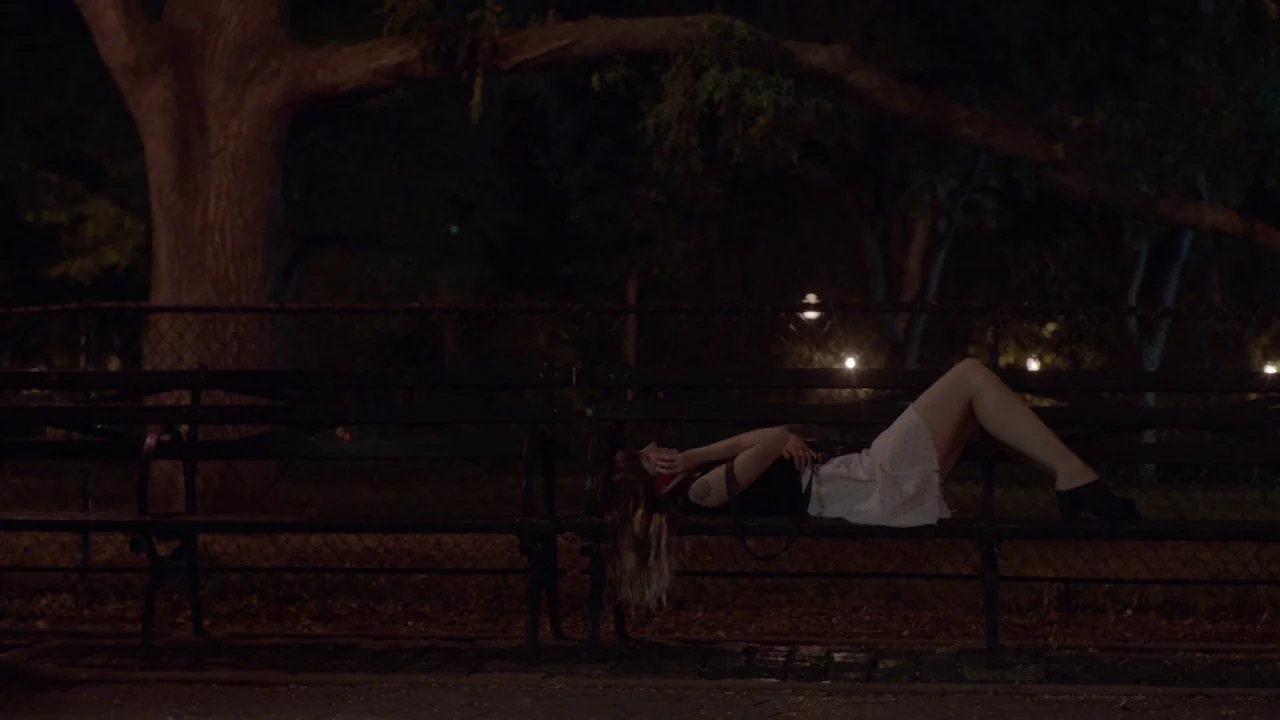The Heart Machine (2014) movie still: wide — A nighttime park scene features a dark bench situated under a large tree. A young woman lies…