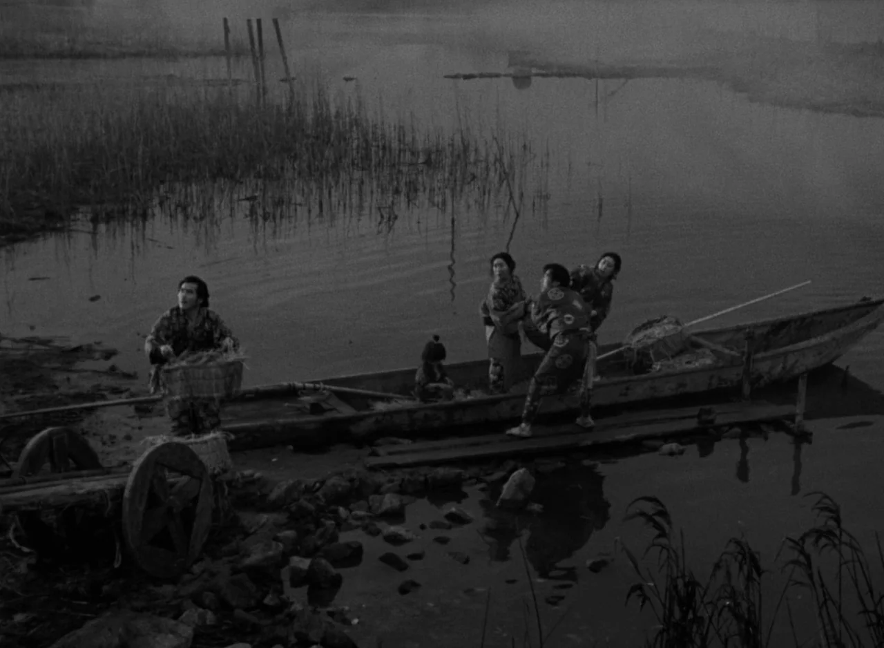 Ugetsu (1953) movie still: wide — A misty riverbank at dawn with a wooden boat moored to the shore. Five people in traditional clothing move items…