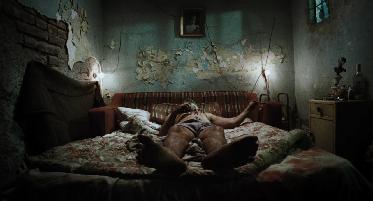 Amores Perros (2000) movie still: medium — A dilapidated bedroom features walls with peeling paint and a faded striped sofa-bed. An older man lies…