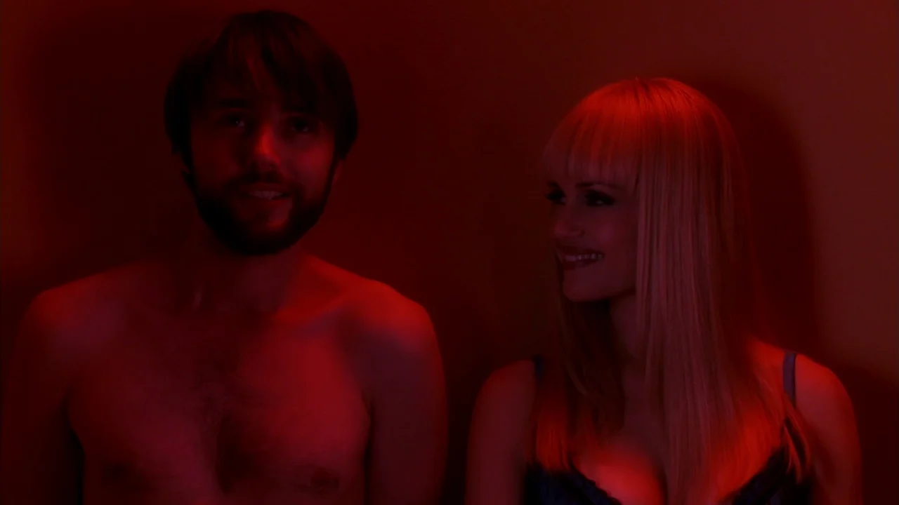 Electra Luxx (2010) movie still: medium — A dark indoor space is filled with intense red light. A young man and woman look at each other while…