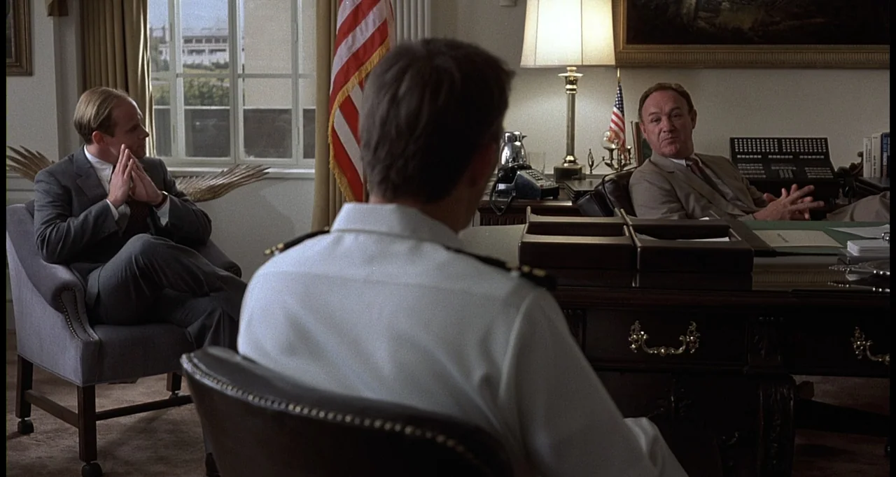 No Way Out (1987) movie still: medium — A formal office with a desk, leather chairs, and an American flag. Three men sit in chairs while one man…