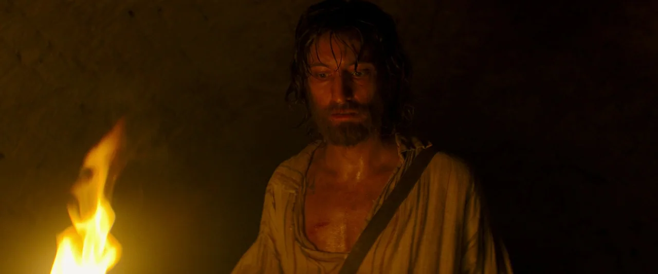 The Count of Monte-Cristo (2024) movie still: medium — A dark, windowless stone chamber is lit only by the flickering glow of a torch. A disheveled…