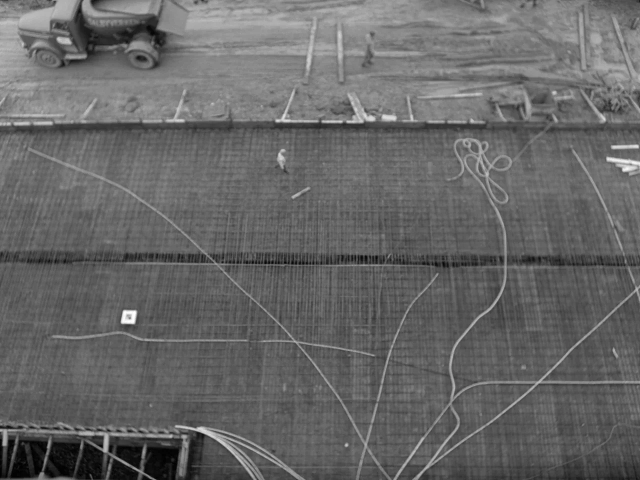The Baby Carriage (1963) movie still: establishing — An overhead view of a large concrete slab reinforced with a metal rebar grid. A dump truck…