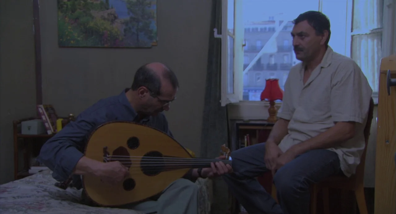 The Secret of the Grain (2007) movie still: medium — A spare, dimly lit room contains a bed and a view through an open window. One man sits on the…