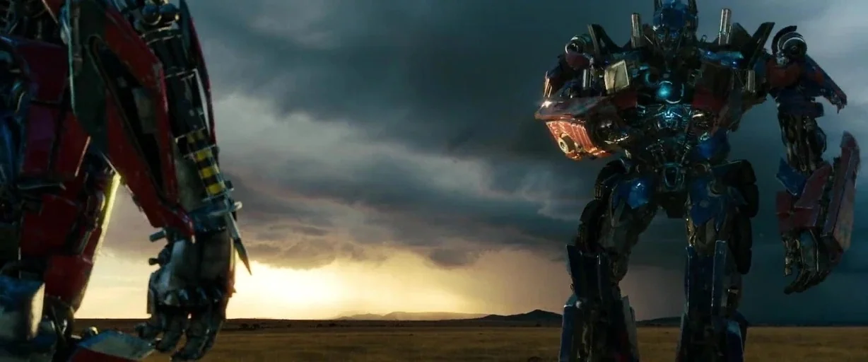 Transformers: Dark of the Moon (2011) movie still: wide — Two giant robotic creatures stand in a vast open field under a dark storm sky. The sun…