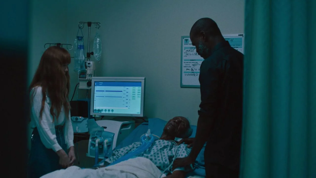 She Dies Tomorrow (2020) movie still: medium — A dimly lit hospital room features a patient resting in a hospital bed. A young woman and a man stand…