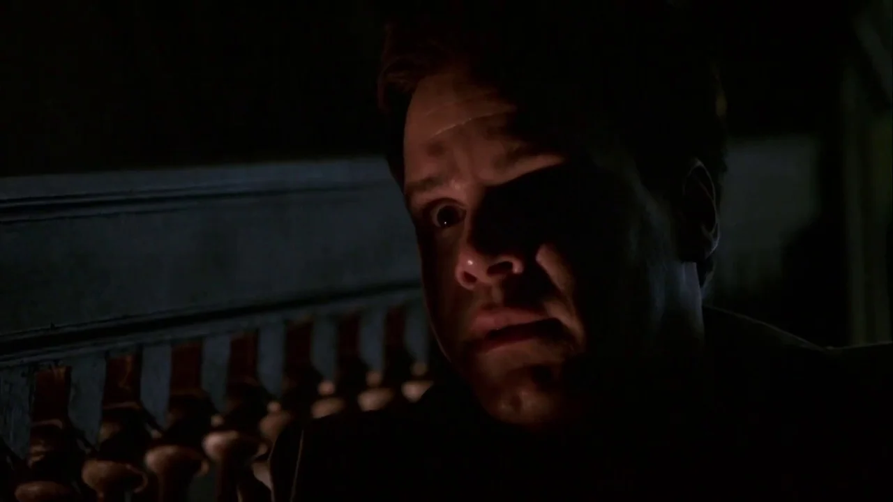 Hellraiser: Inferno (2000) movie still: closeup — A man stands in the dark on a wooden porch with decorative railing balusters. The man looks toward…
