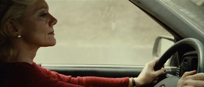 The Headless Woman (2008) movie still: medium — A woman drives a car along a road during the daytime. She looks straight ahead while keeping both…