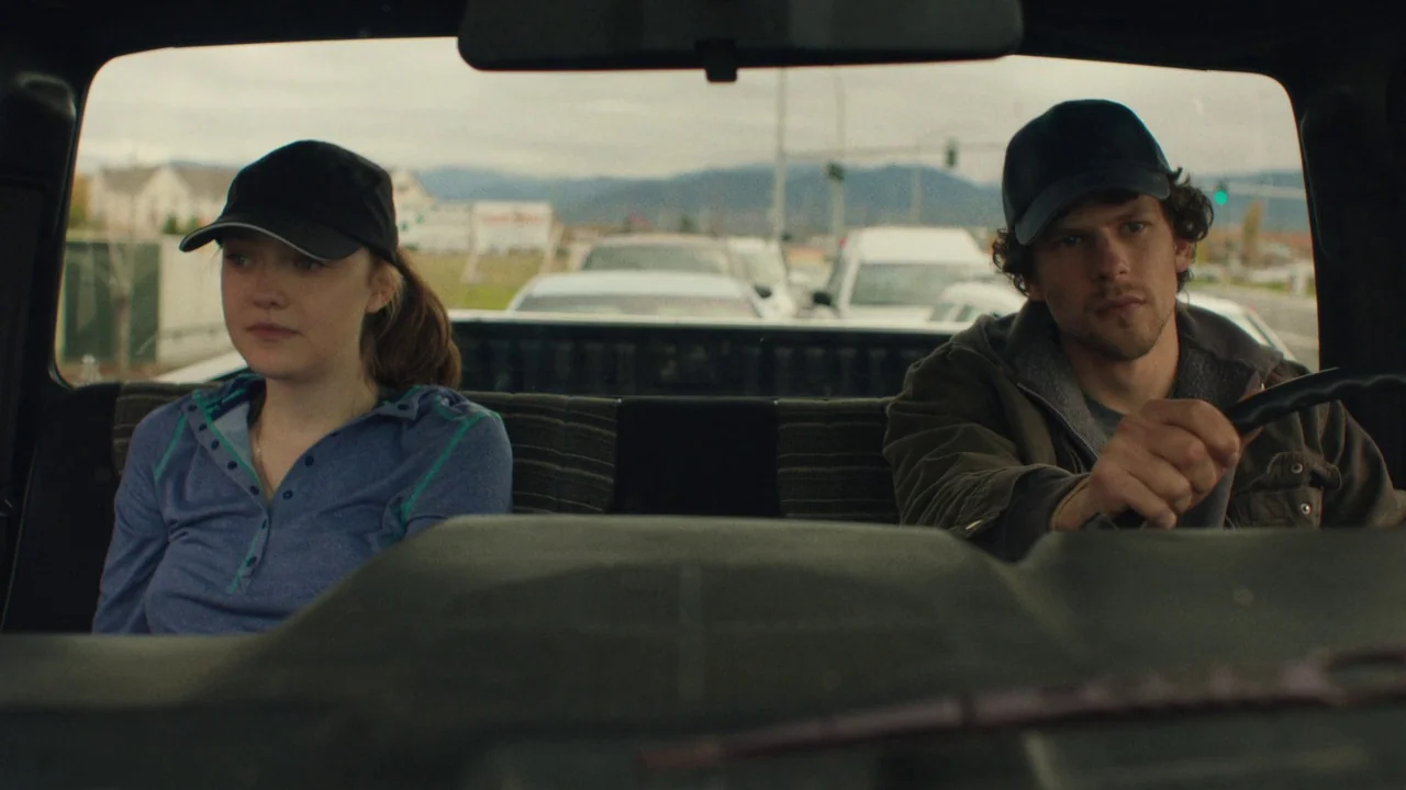 Night Moves (2013) movie still: medium — A man and woman sit in the front seats of a vehicle interior. The man steers while the woman watches the…