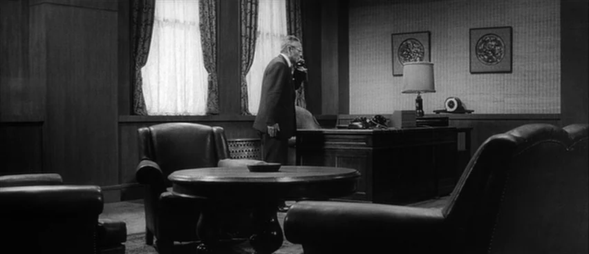 The Bad Sleep Well (1960) movie still: wide — A 1950s business space features wood-paneled walls, leather chairs, and two framed wall artworks. An…