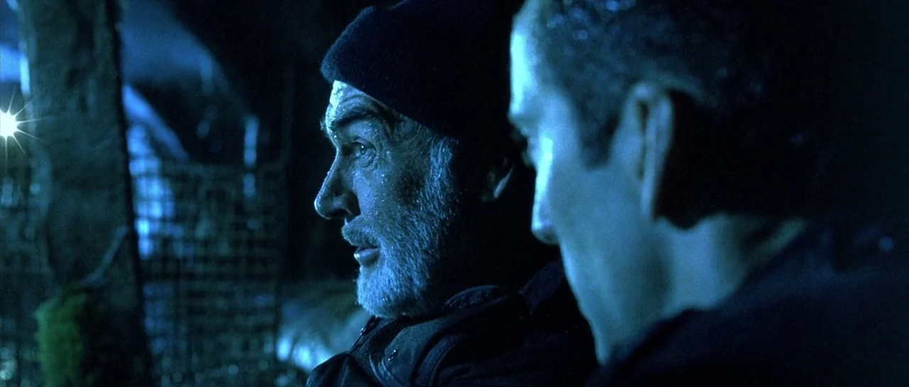 The Rock (1996) movie still: medium — A dark, industrial harbor area at night with metallic structures and mossy surfaces visible. Two men in dark…