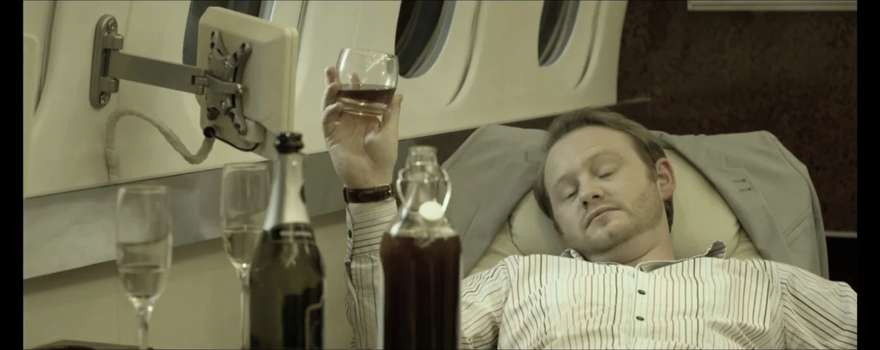 Turbulence (2025) movie still: medium — A man sleeps inside a private airplane cabin with oval windows and padded upholstery. He reclines in his…