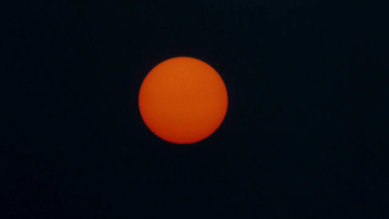 The Exorcist 3 (1990) movie still: wide — The bright orange sun is centered in a dark, empty expanse of sky. No clouds or other features are visible…