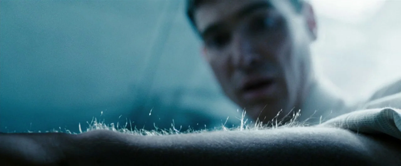 Watchmen (2009) movie still: closeup — A sterile environment with cool blue lighting focused on a man in a gown. The subject stares intensely at the…