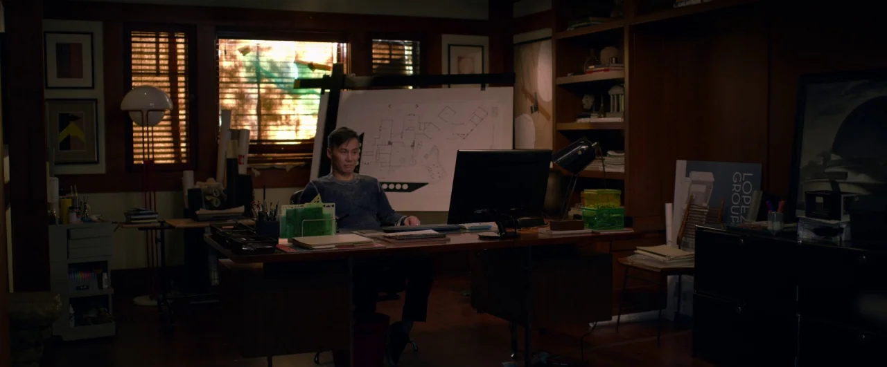 Bird Box (2018) movie still: medium — A dimly lit architectural office features wooden shelving and blueprints against the back wall. An East Asian…
