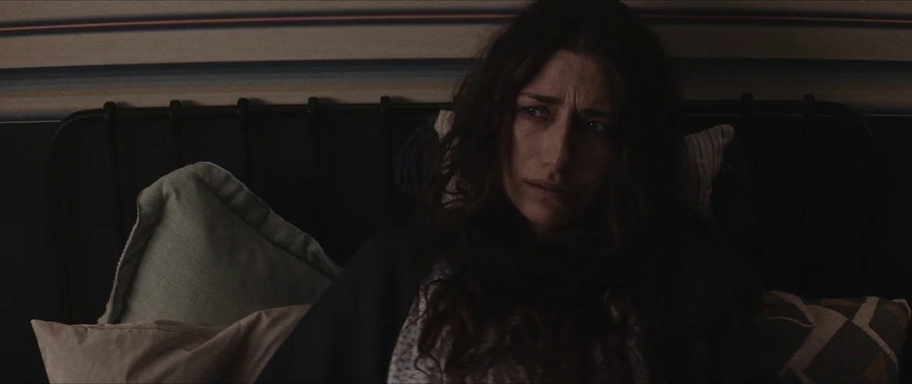 Anything For Jackson (2020) movie still: medium — A woman rests against pillows on a dark metal-framed headboard at night. She looks toward the side…