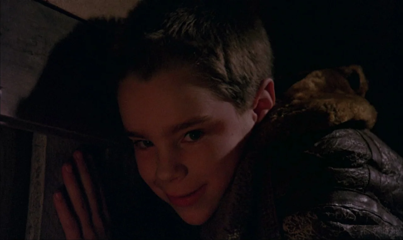 My Life As A Dog (1985) movie still: closeup — A dark, cramped indoor space with textured wall surfaces and limited ambient light. A young boy leans…
